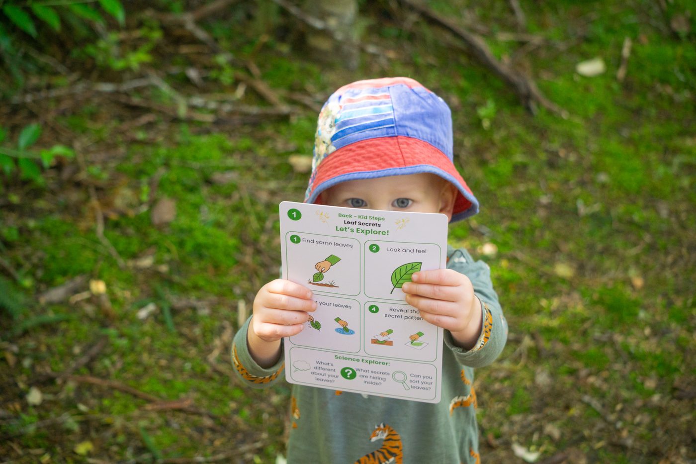 A child in the bush holding up a Wild Wonders activity card